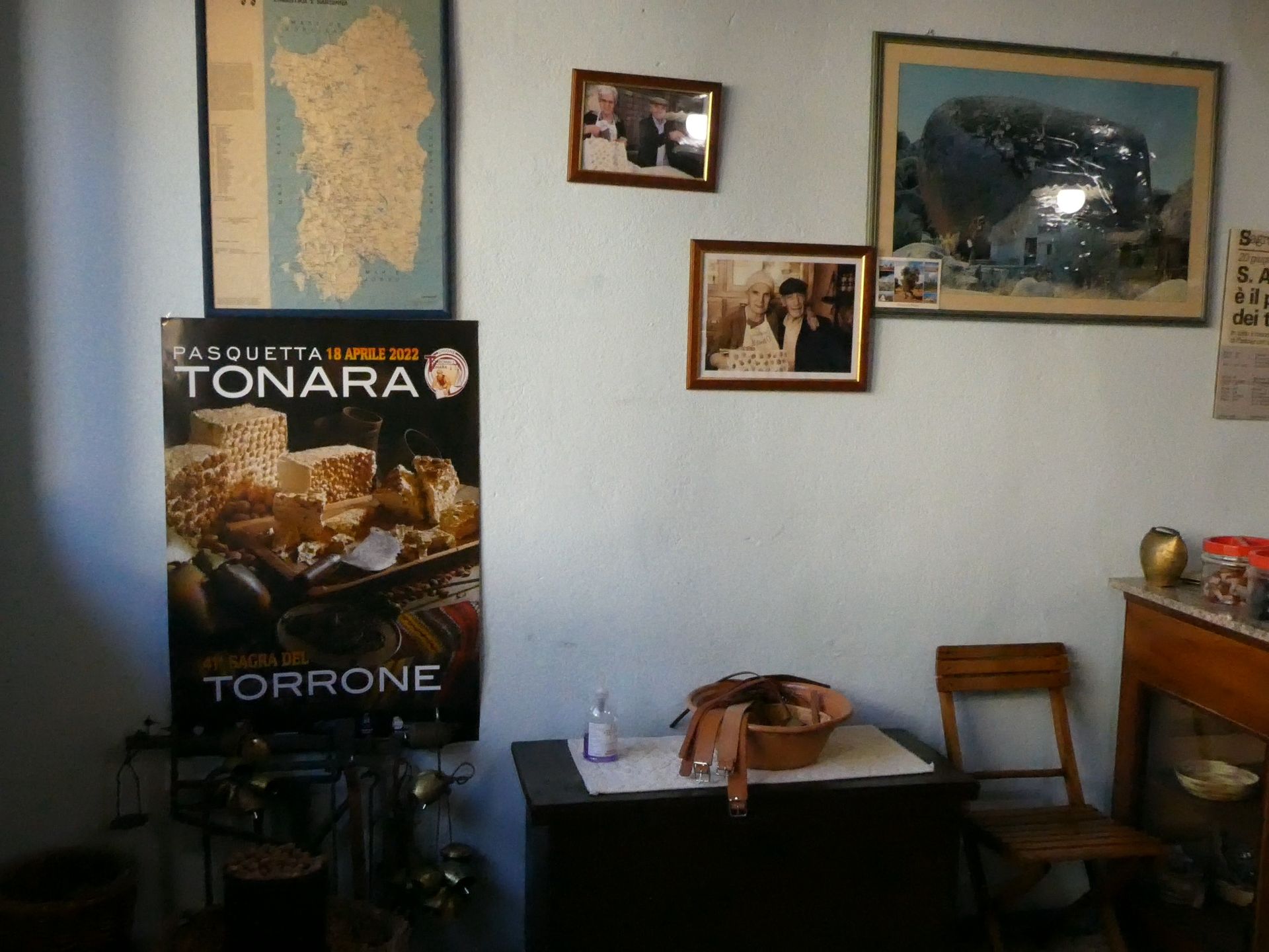Interno con poster e foto incorniciate su una parete azzurra, un tavolo con un cestino e una sedia di legno.