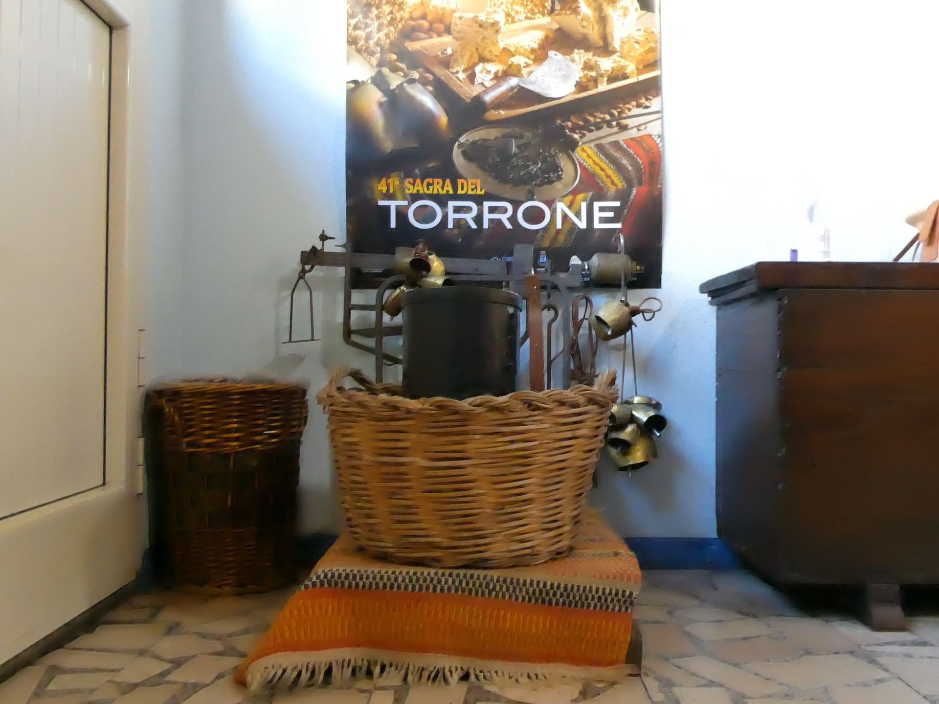 Cestino di vimini su coperta arancione con utensili da cucina, cassapanca in legno e poster nella stanza.