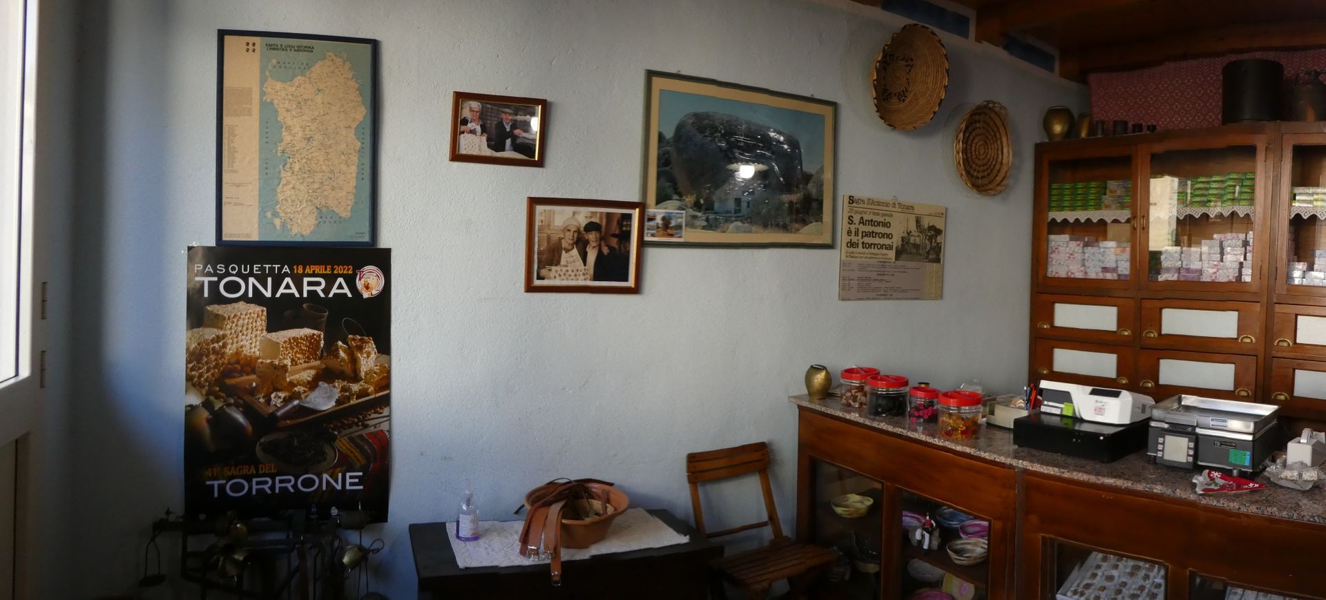 Interno di un negozio con una mappa e quadri incorniciati alle pareti. Un bancone espositivo è pieno di merce.