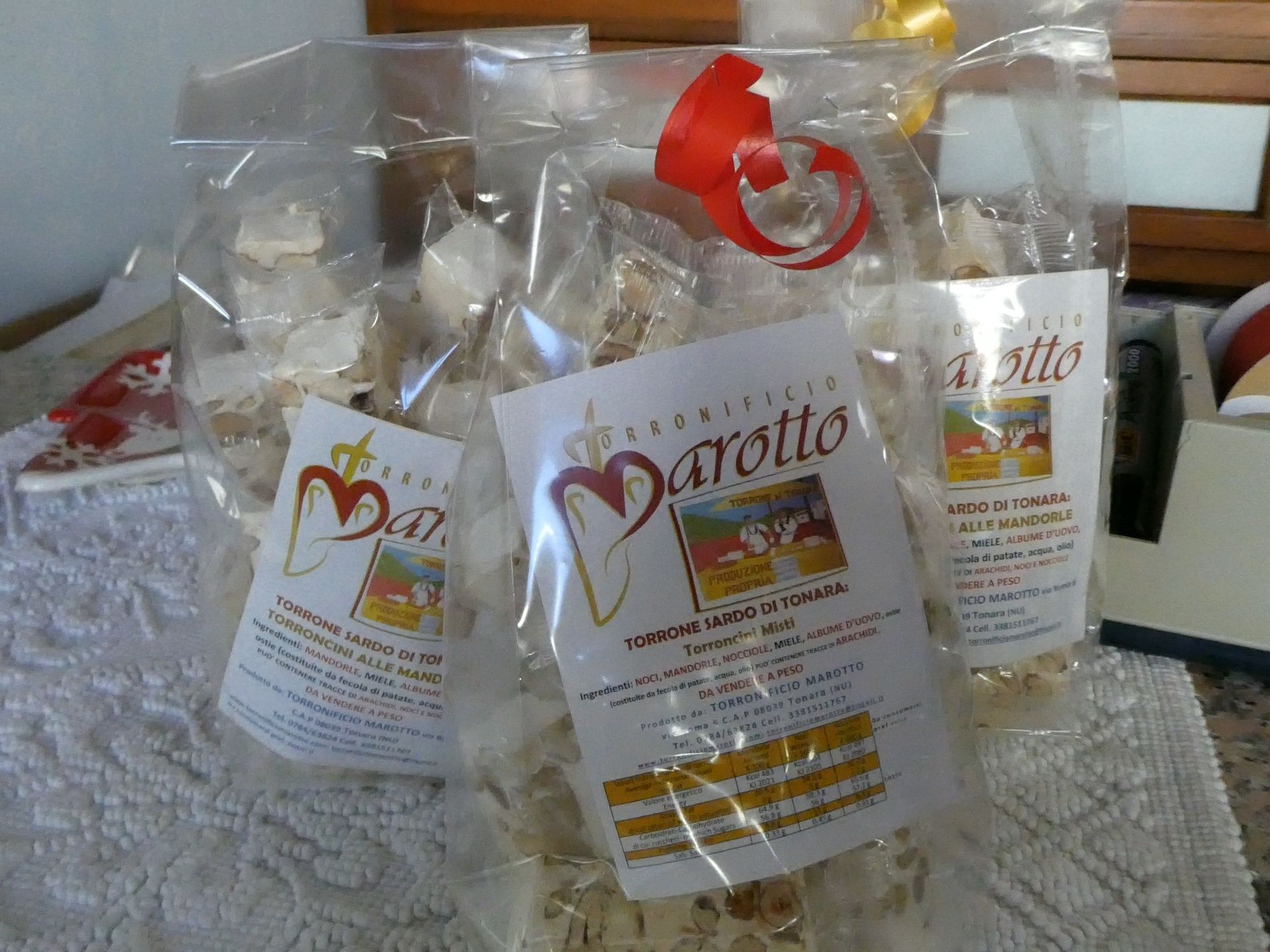 Tre sacchetti di cellophane contenenti torrone bianco con etichette personalizzate, legati con un nastro rosso, su una superficie di colore chiaro.