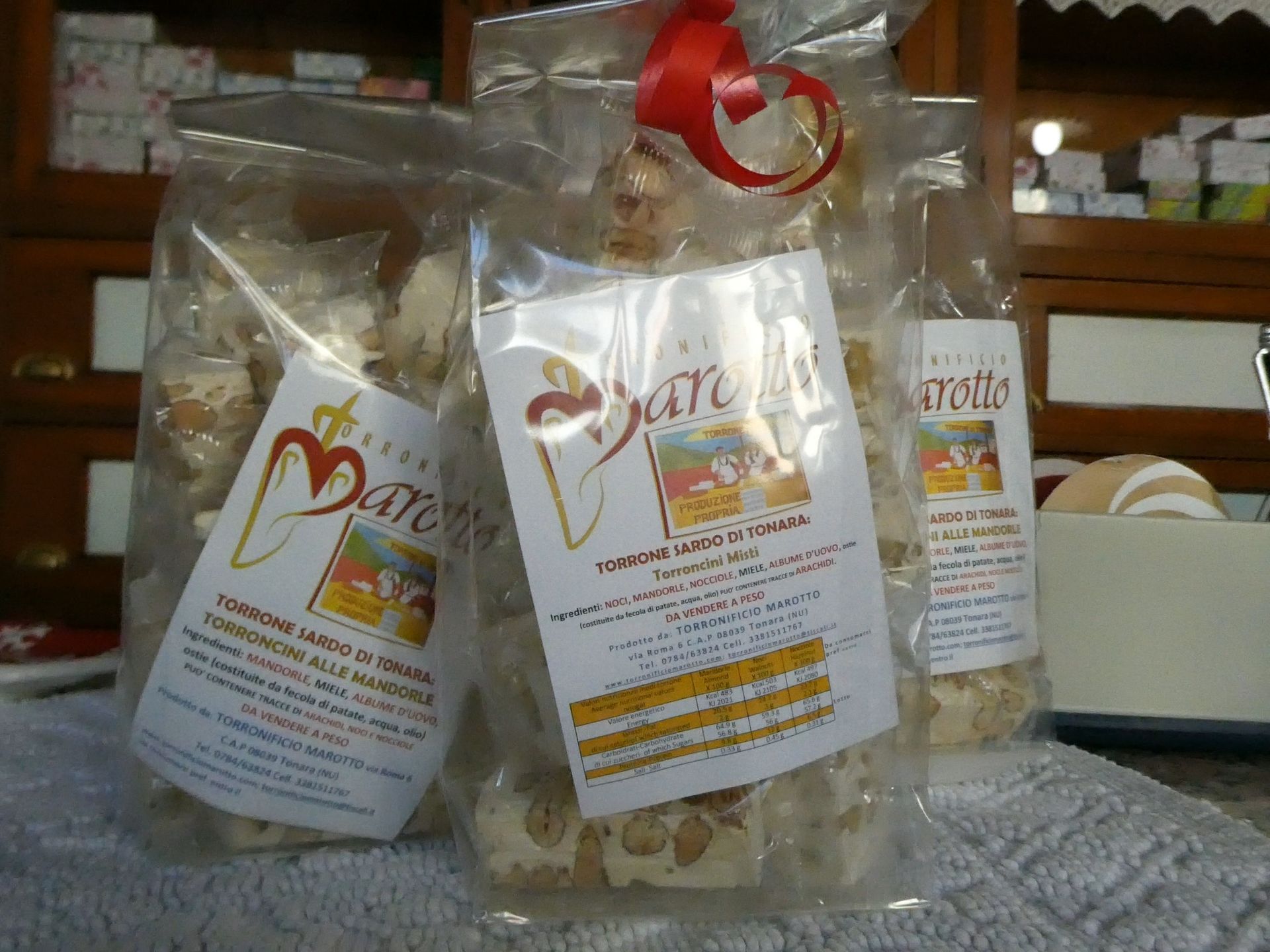 Sacchetti di torrone con etichette, legati con un nastro rosso. Esposti su uno scaffale insieme ad altri articoli.