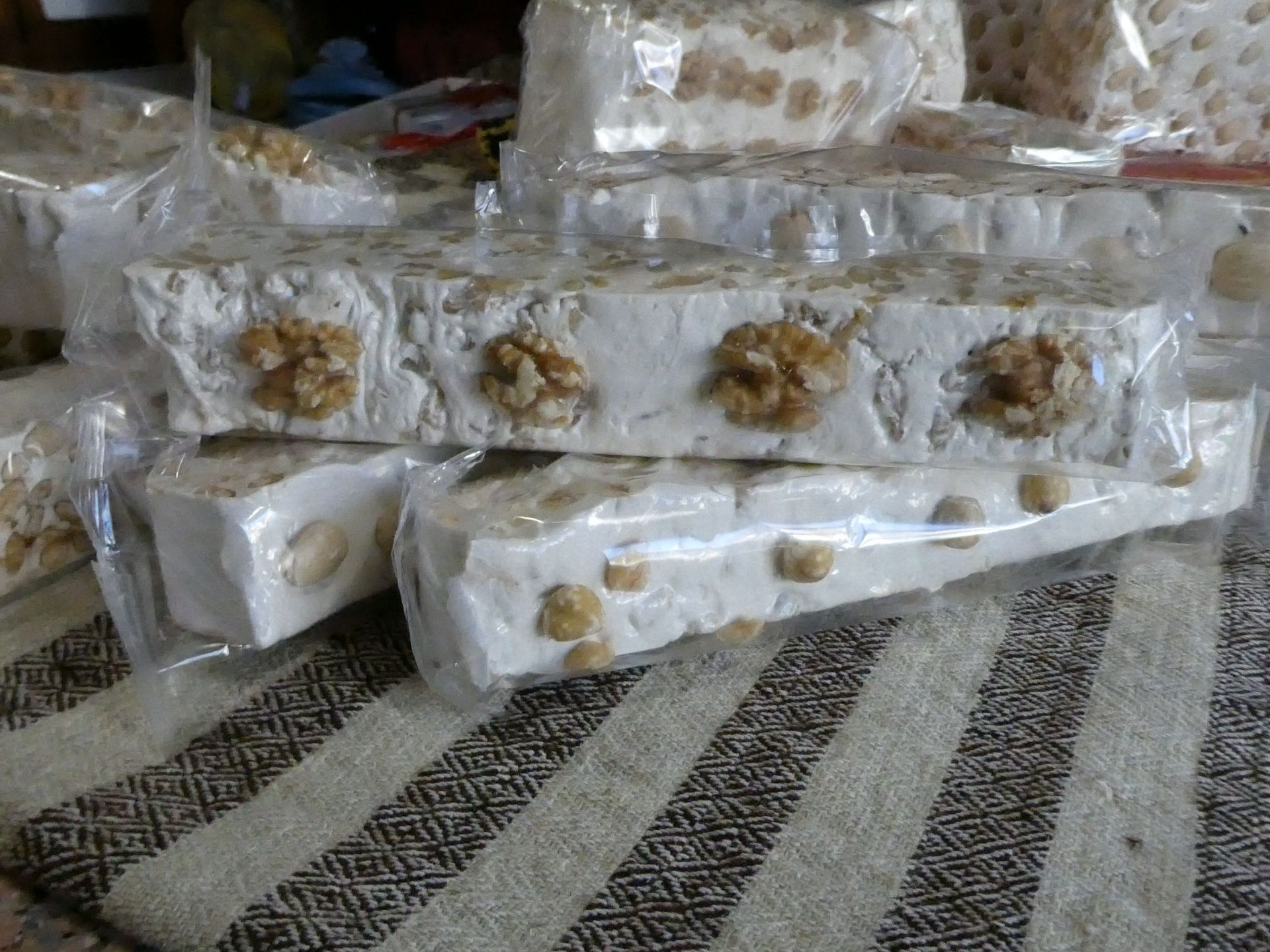 Blocchi di torrone confezionati con noci su una superficie con motivo intrecciato.