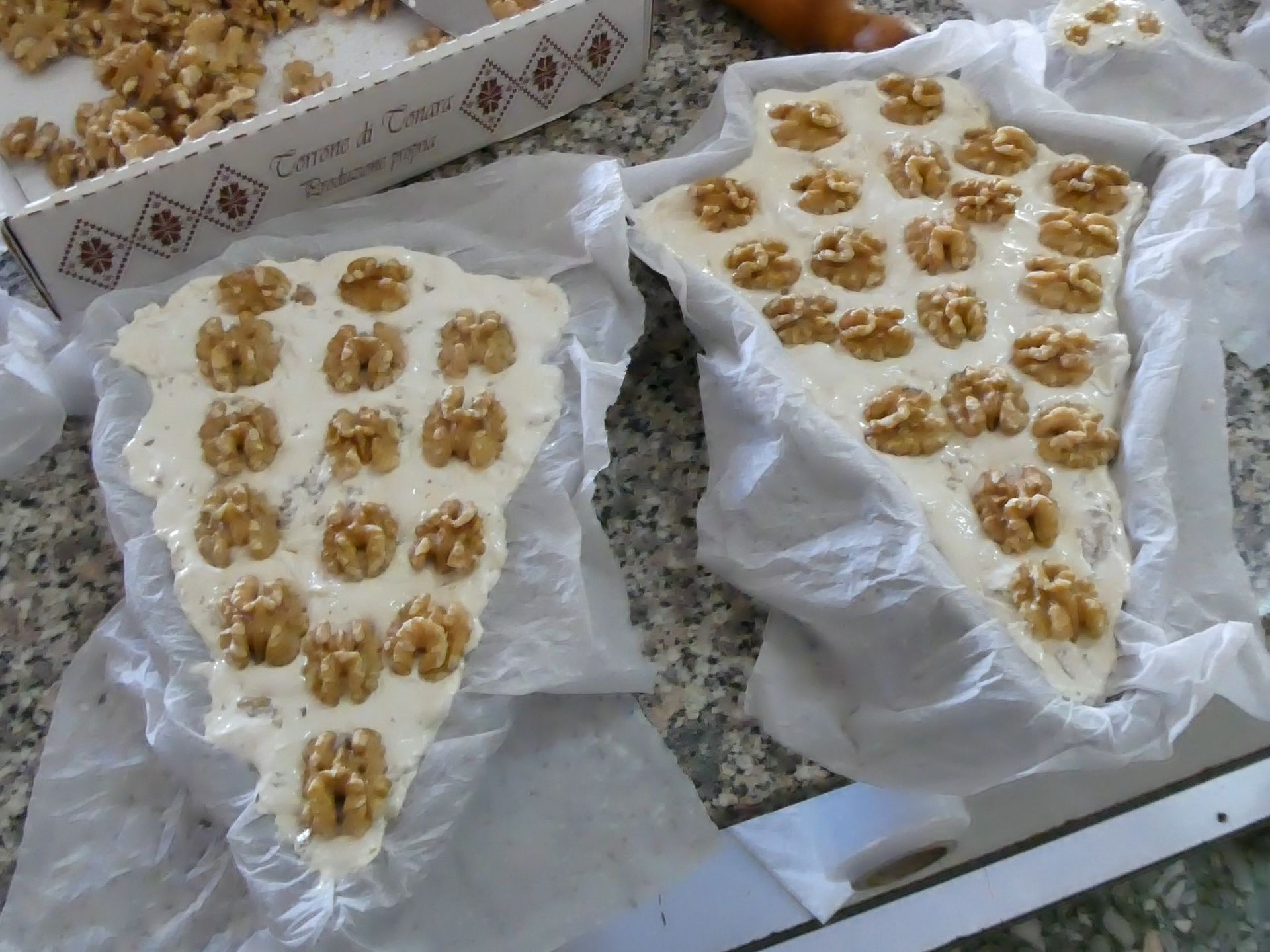 Due dolci piatti e bianchi, ricoperti di noci, in vassoi rivestiti di carta.