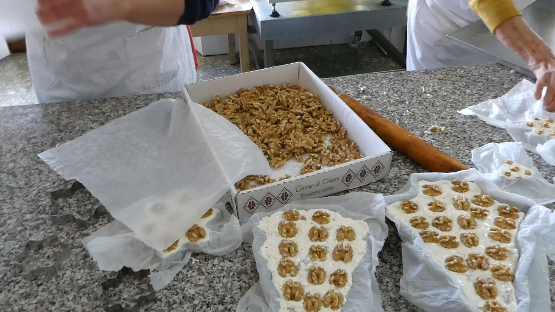 Pasticceri che preparano il torrone alle noci. Scatola di noci, tavolette di torrone sul tavolo, avvolte nella carta.