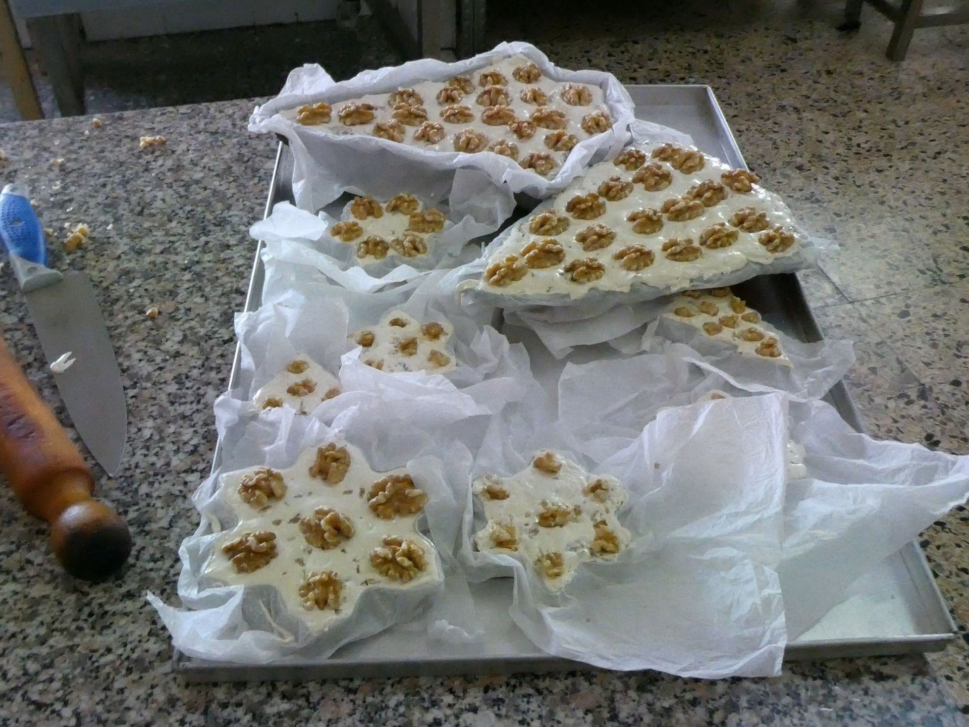 Vassoio di pasticcini, ognuno guarnito con noci, appoggiato su carta bianca. Ambiente da cucina.