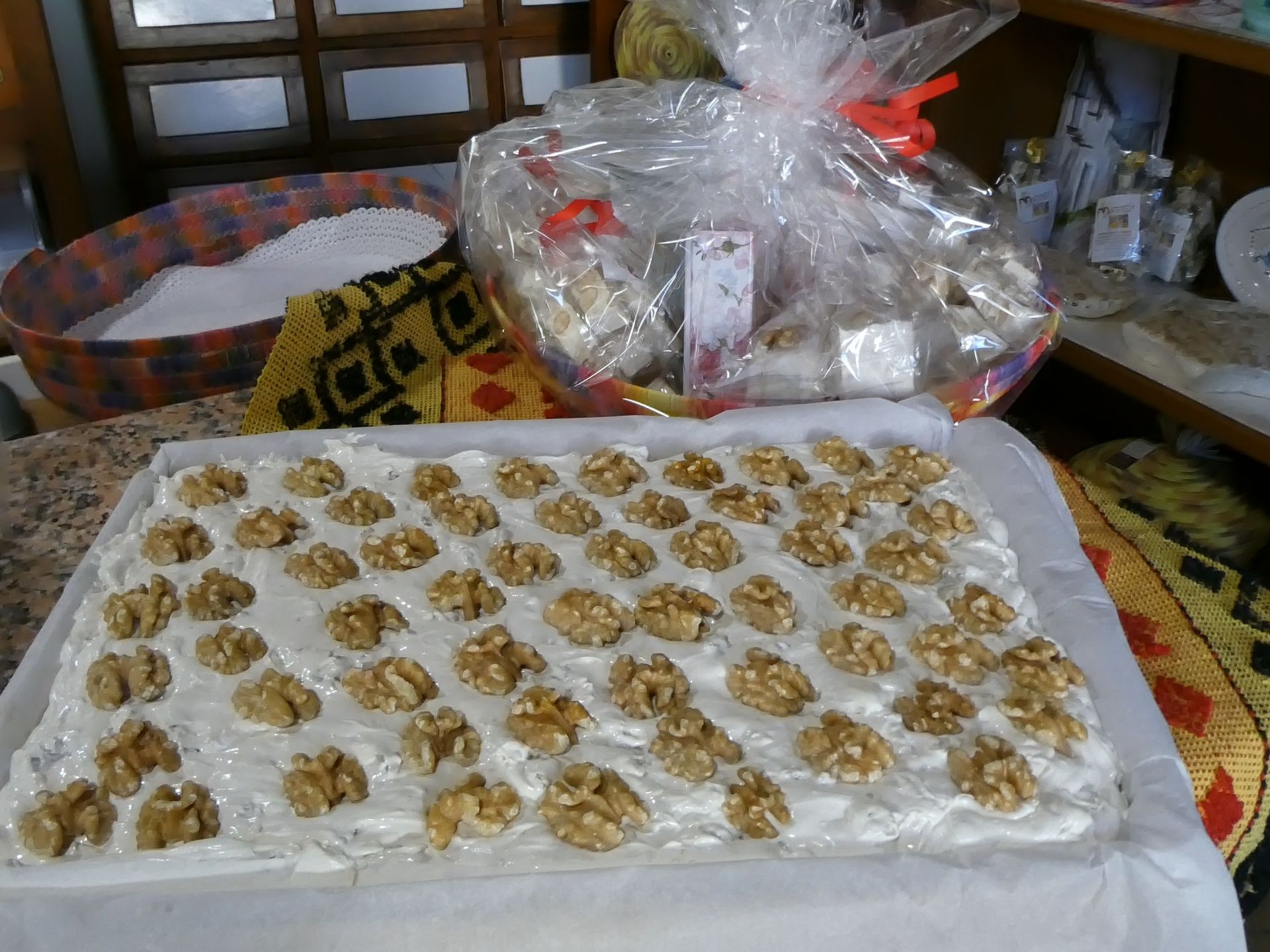 Vassoio di dolciumi bianchi con noci, accanto a un cesto regalo e a uno scaffale espositivo.