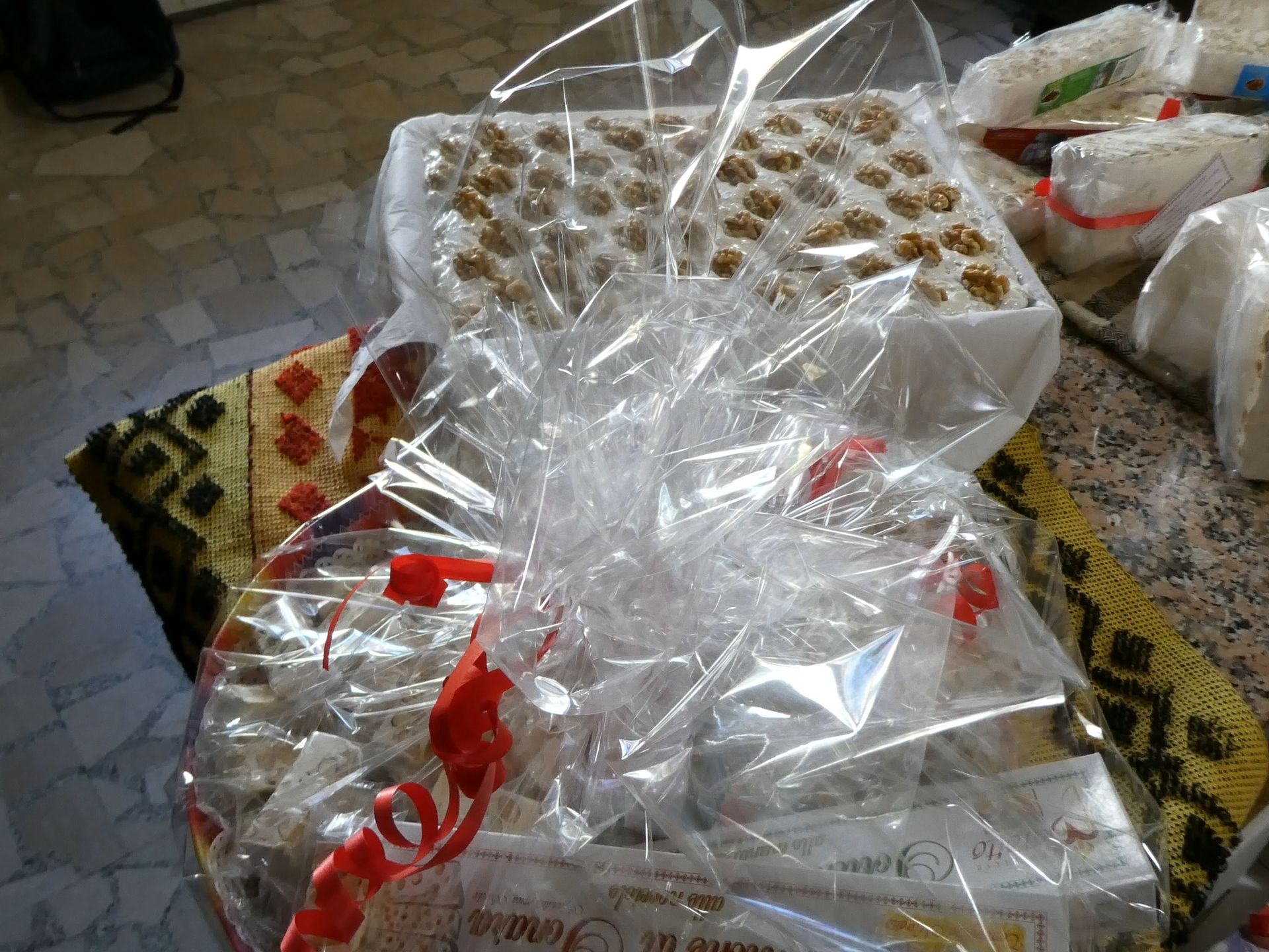 Cesto regalo avvolto in cellophane trasparente con nastro rosso, contenente dolciumi guarniti con noci.
