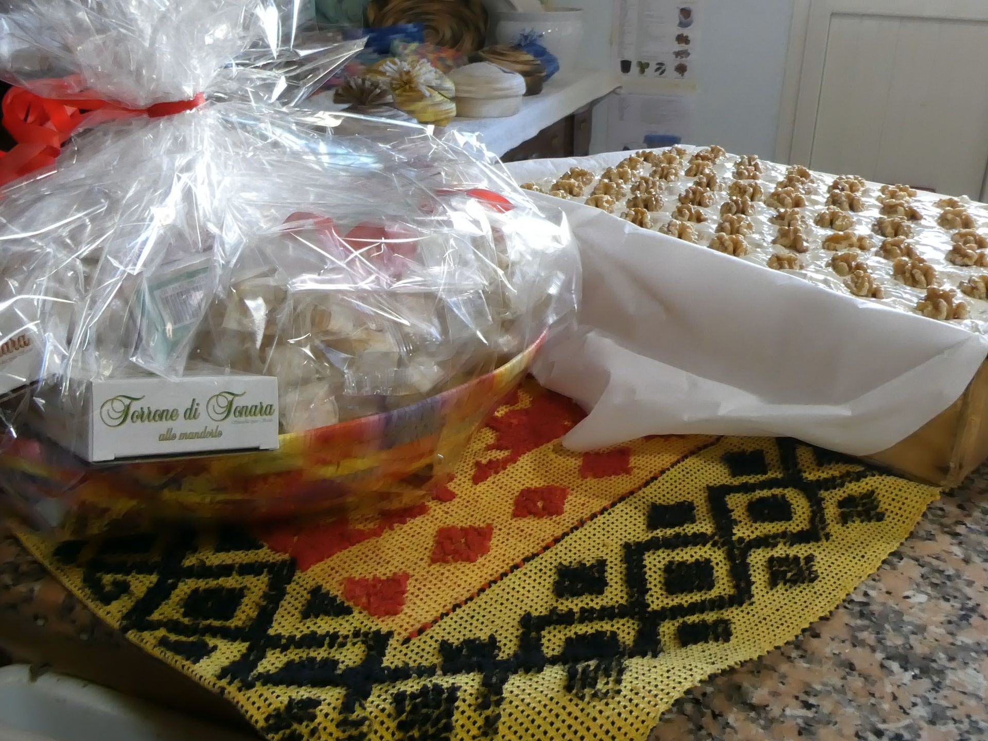 Cestino di dolcetti incartati e vassoio di quadrati glassati con noci su stoffa fantasia.