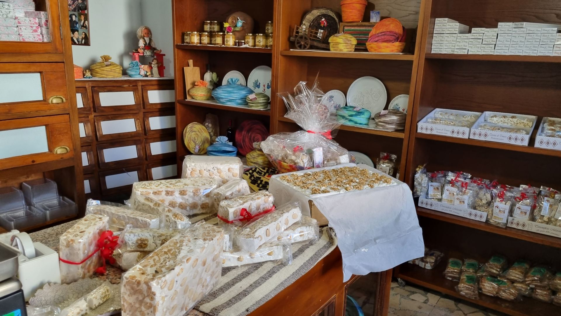 Interno di un negozio con scaffali pieni di prodotti da forno e regali, e pacchetti incartati su un tavolo.