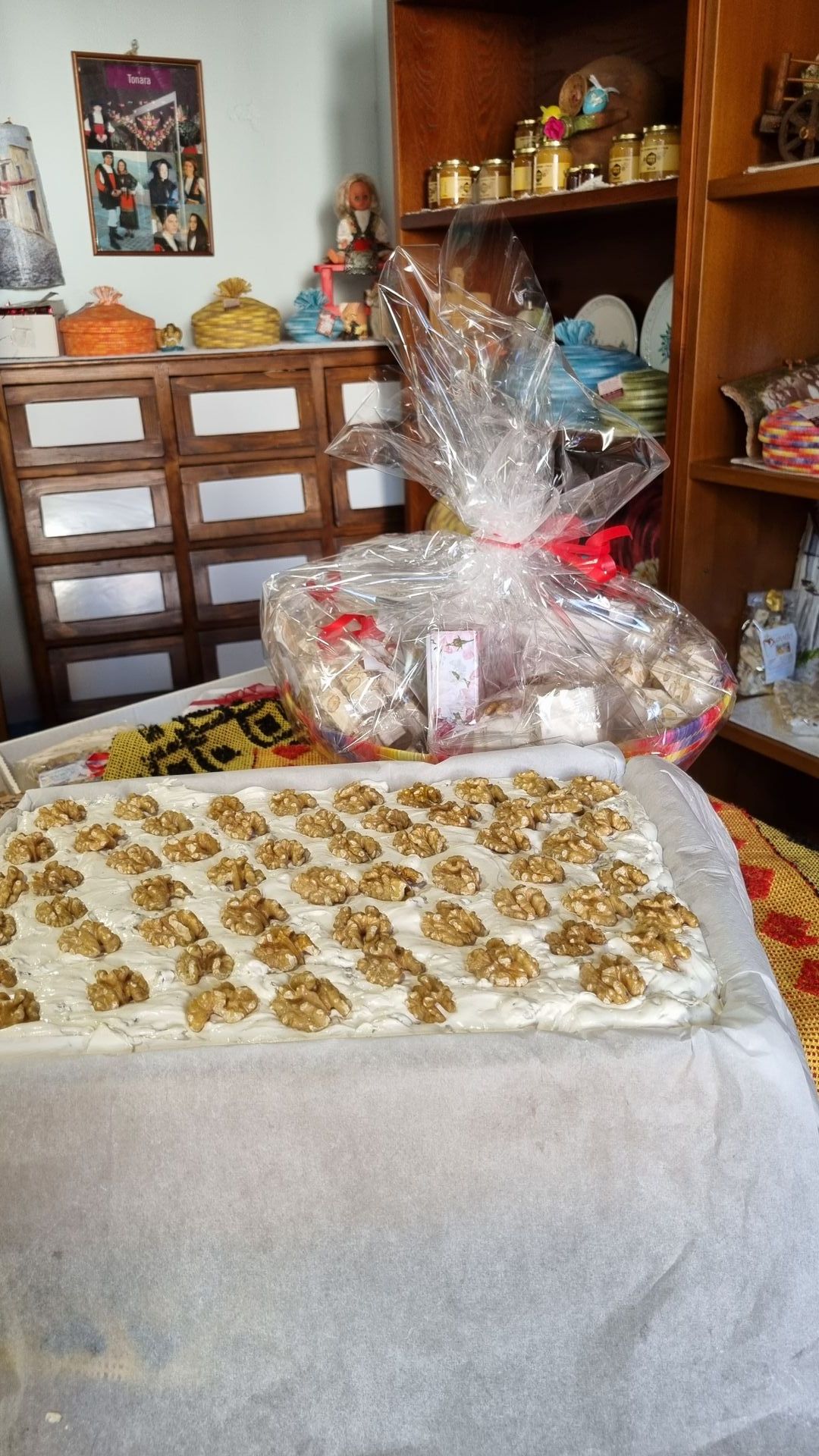 Vassoio di dessert con guarnizione in noce, cesto regalo avvolto in cellophane, ripiani in legno sullo sfondo.