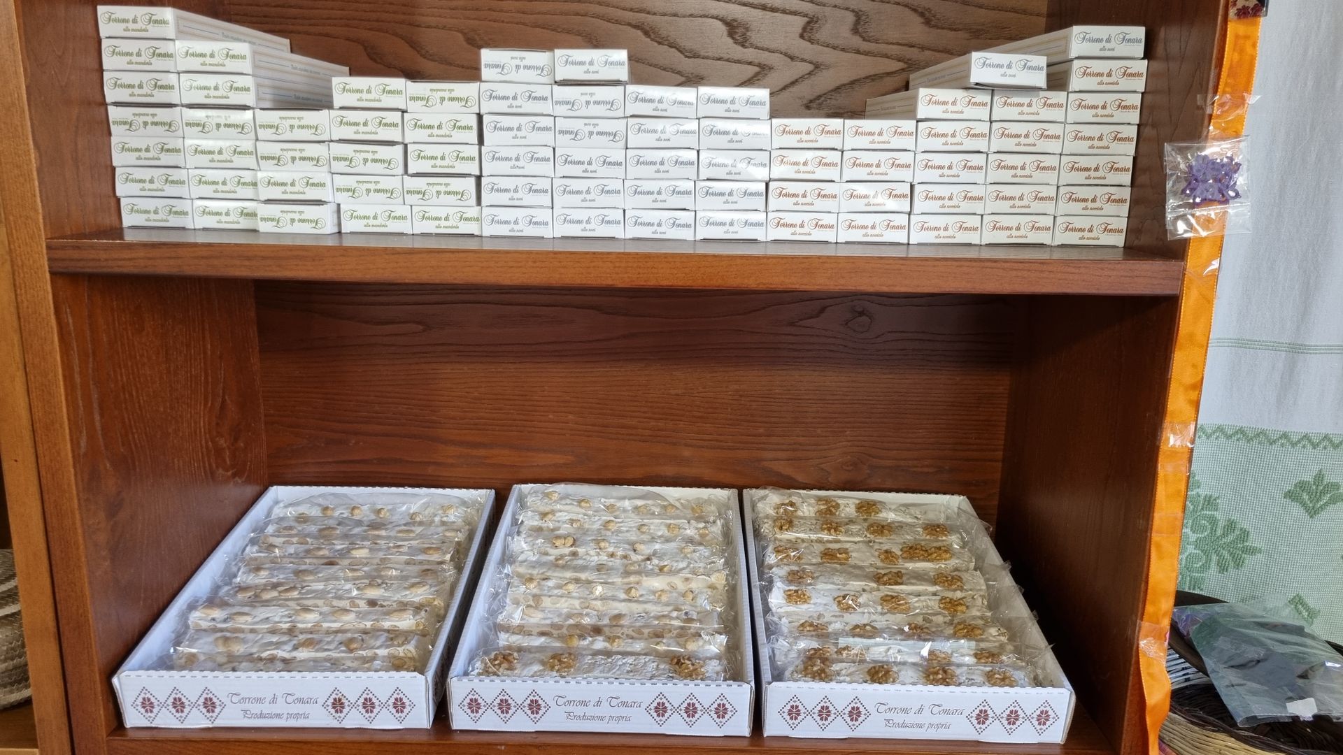 Mensola in legno con piccole scatole con testo, sopra vassoi di cibo confezionato.