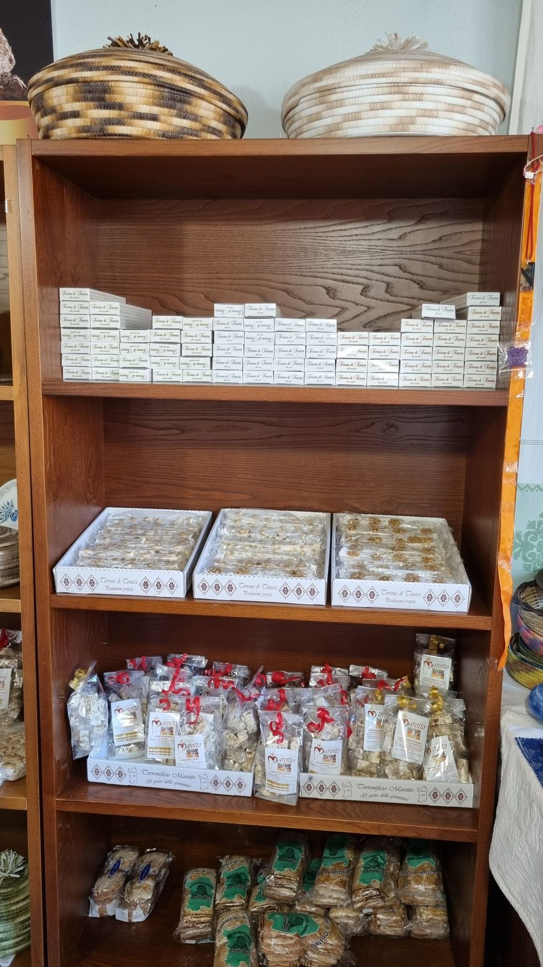 Scaffale in legno pieno di alimenti confezionati; due cestini sul ripiano superiore.