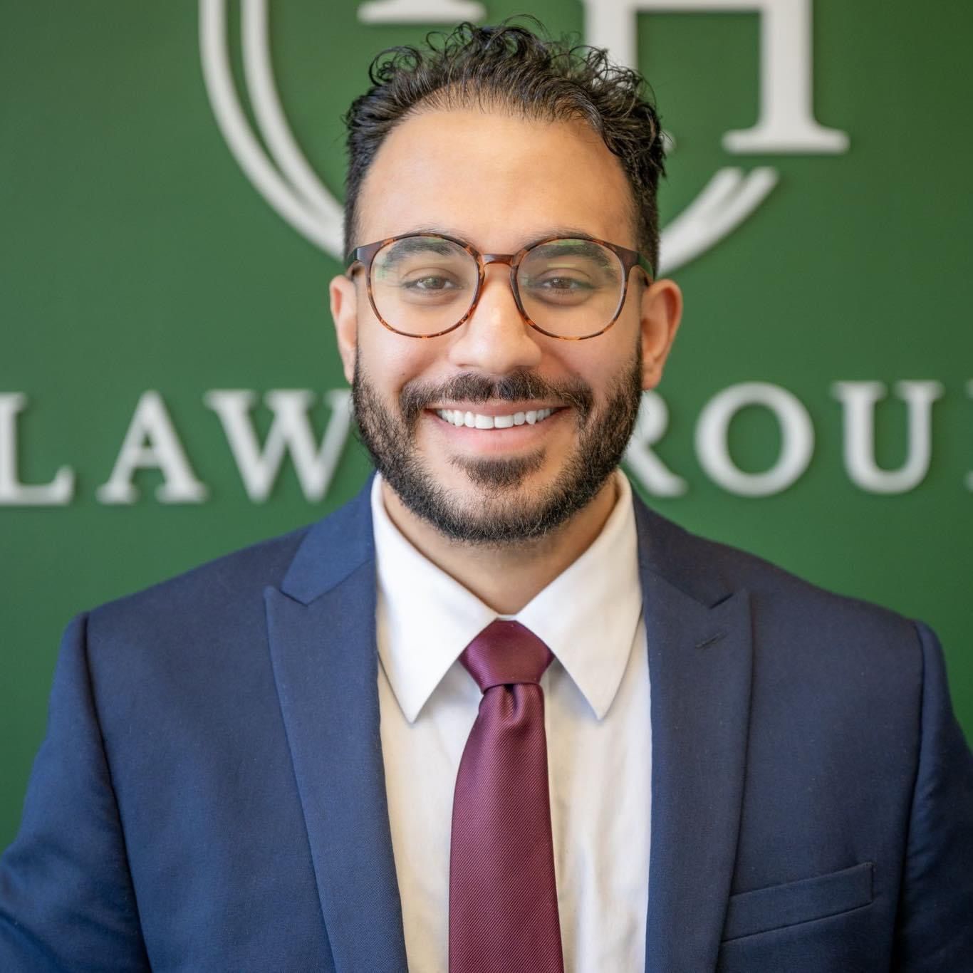 Man in suit and glasses smiling in front of a green wall with