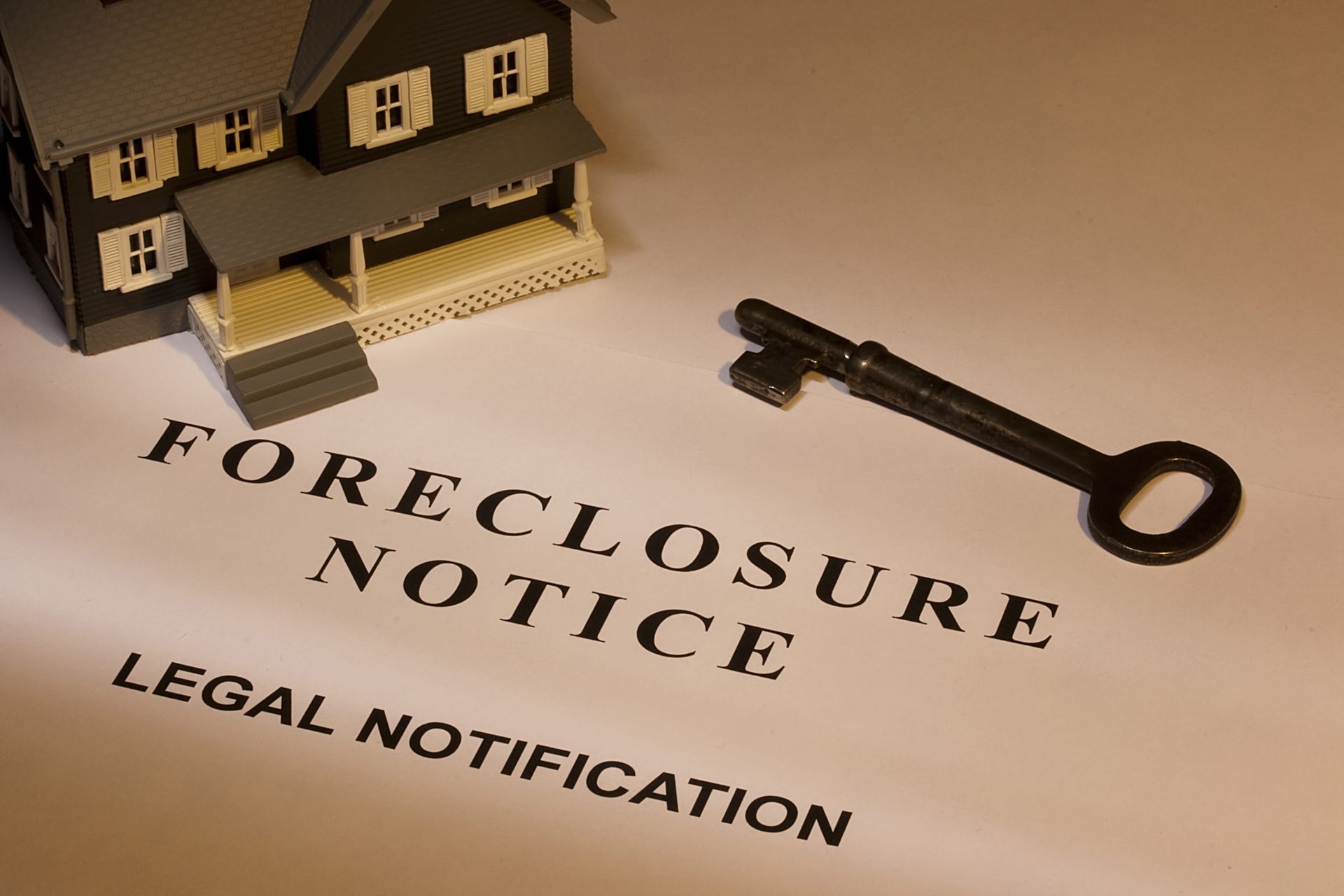 Foreclosure notice beside a house model and key on a table