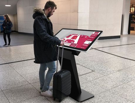 A man with a suitcase is standing in front of a large screen.