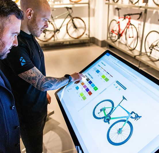 Two men are looking at a screen with a bicycle on it