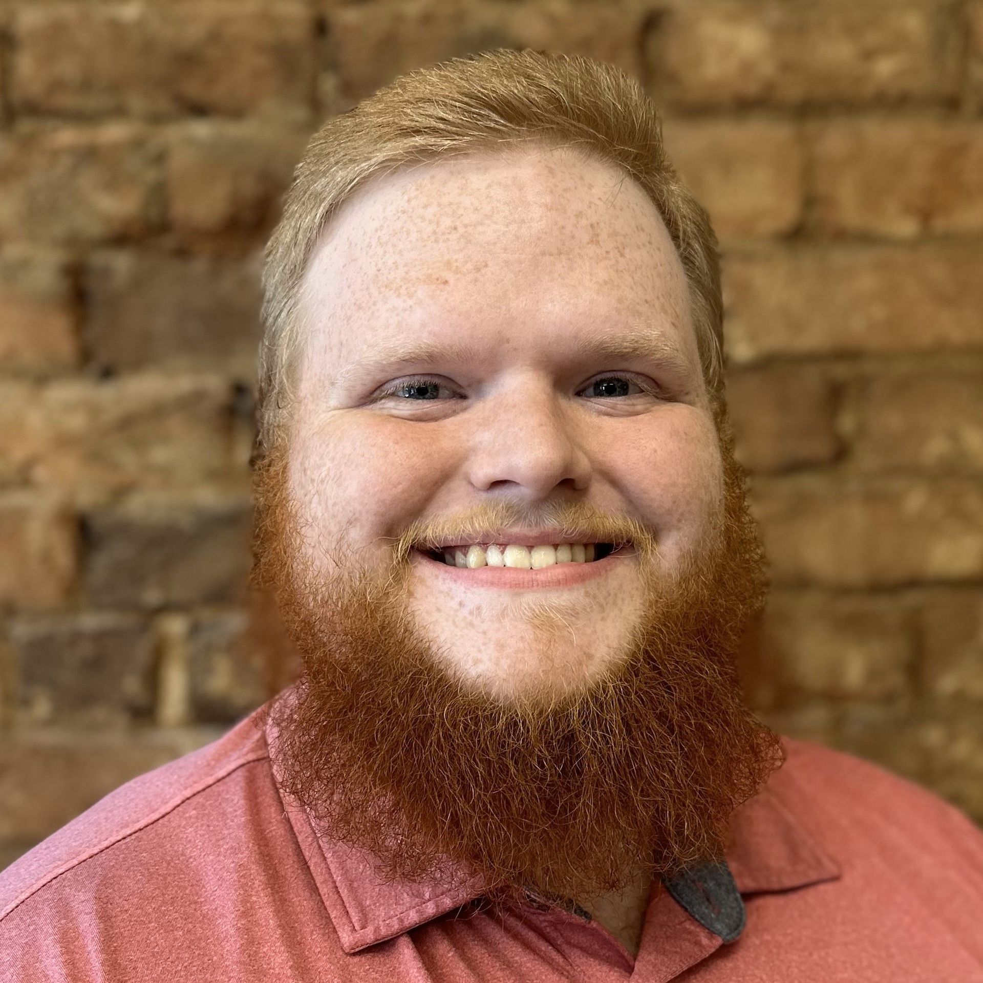 A man with a beard is smiling in front of a brick wall.