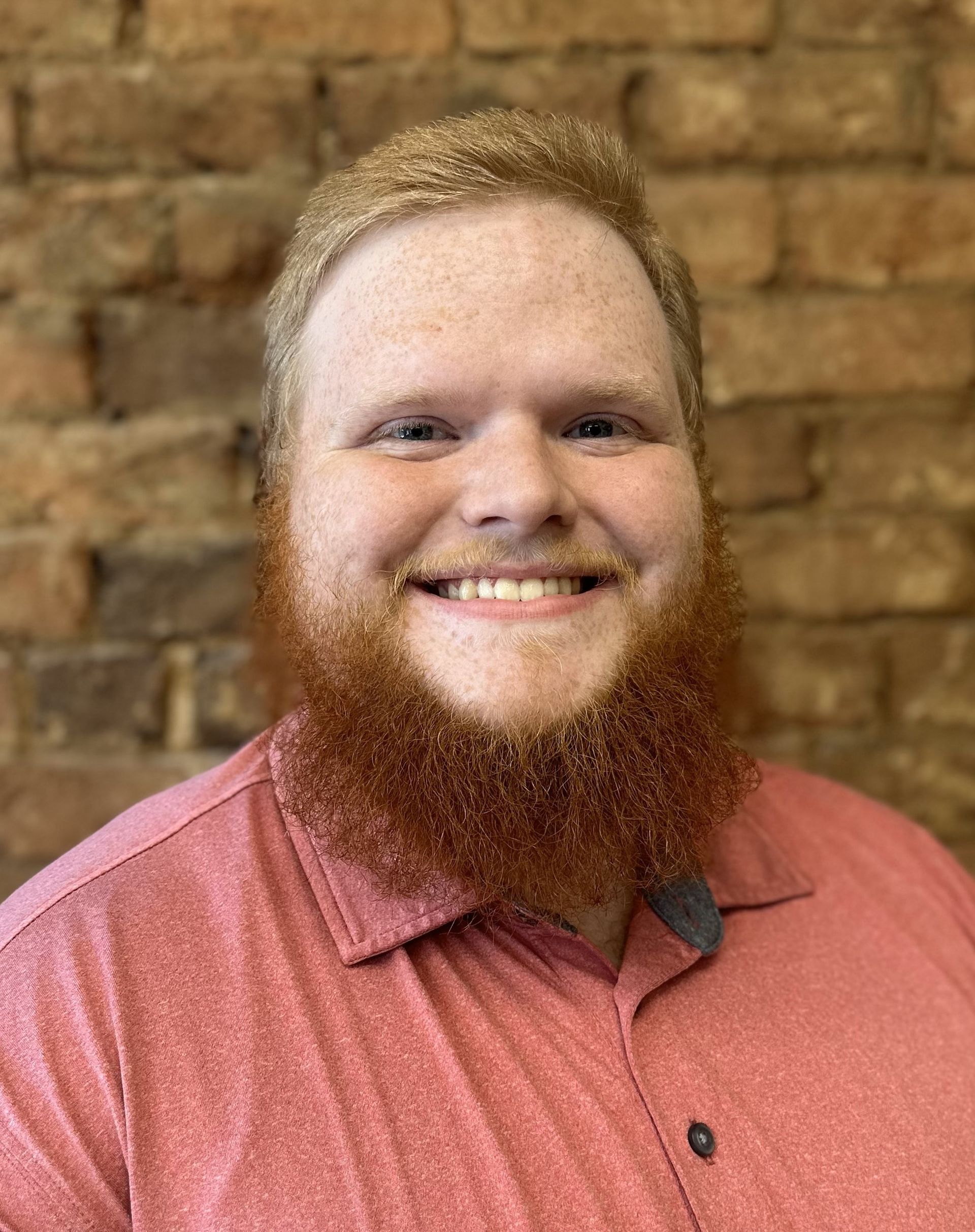 A man with a beard is smiling in front of a brick wall.