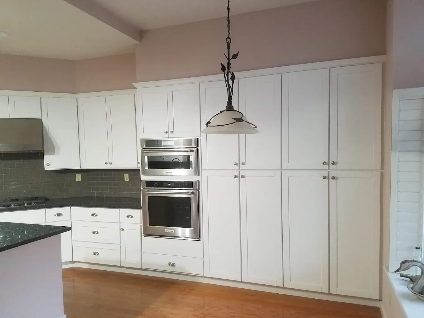 White kitchen cabinets with built-in oven and stovetop.  A decorative light fixture hangs in the center.
