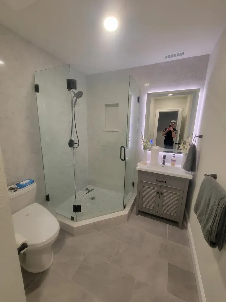 Modern bathroom with glass shower, gray vanity, toilet, and gray tile floor.