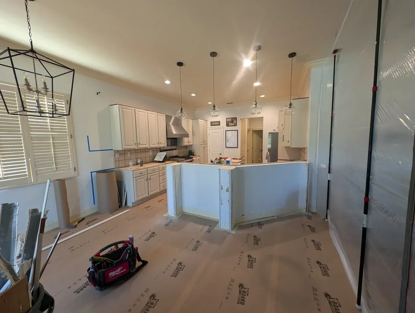 Kitchen under construction with white cabinets, stainless steel range hood, and pendant lights.