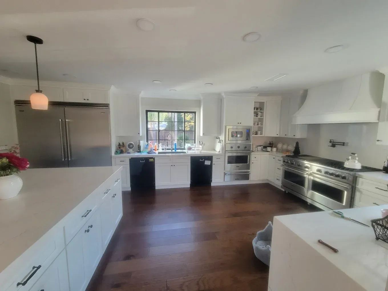 White kitchen with stainless steel appliances, dark wood floors, and a large island.