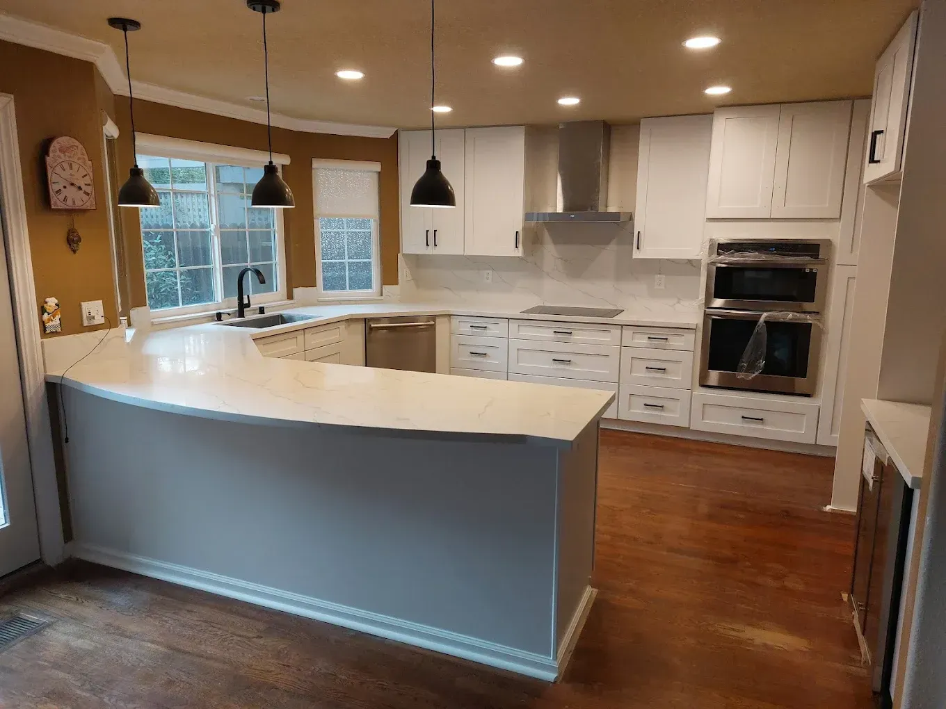 White kitchen with quartz countertops, dark pendant lights, and stainless steel appliances.