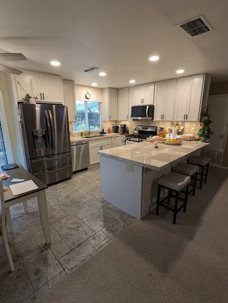 Modern kitchen with white cabinets, stainless steel appliances, and a central island with stools.