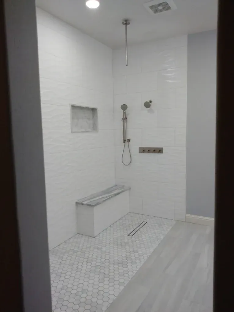 White tile shower with built-in bench, hexagon tile floor, and a linear drain.