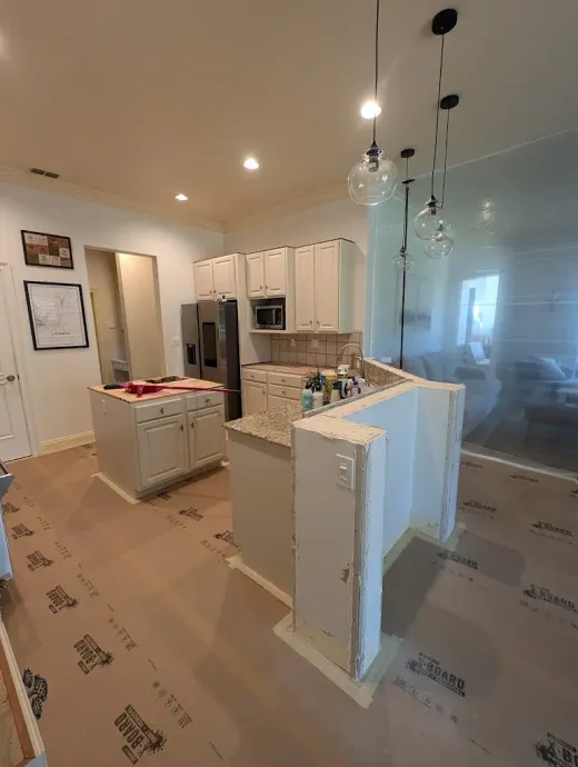 Kitchen with light-colored cabinets and island, stainless steel appliances, and pendant lights. Construction paper covers the floor.