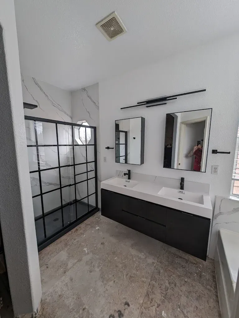Modern bathroom with black framed shower, white walls, dark vanity with two sinks, and large mirrors.