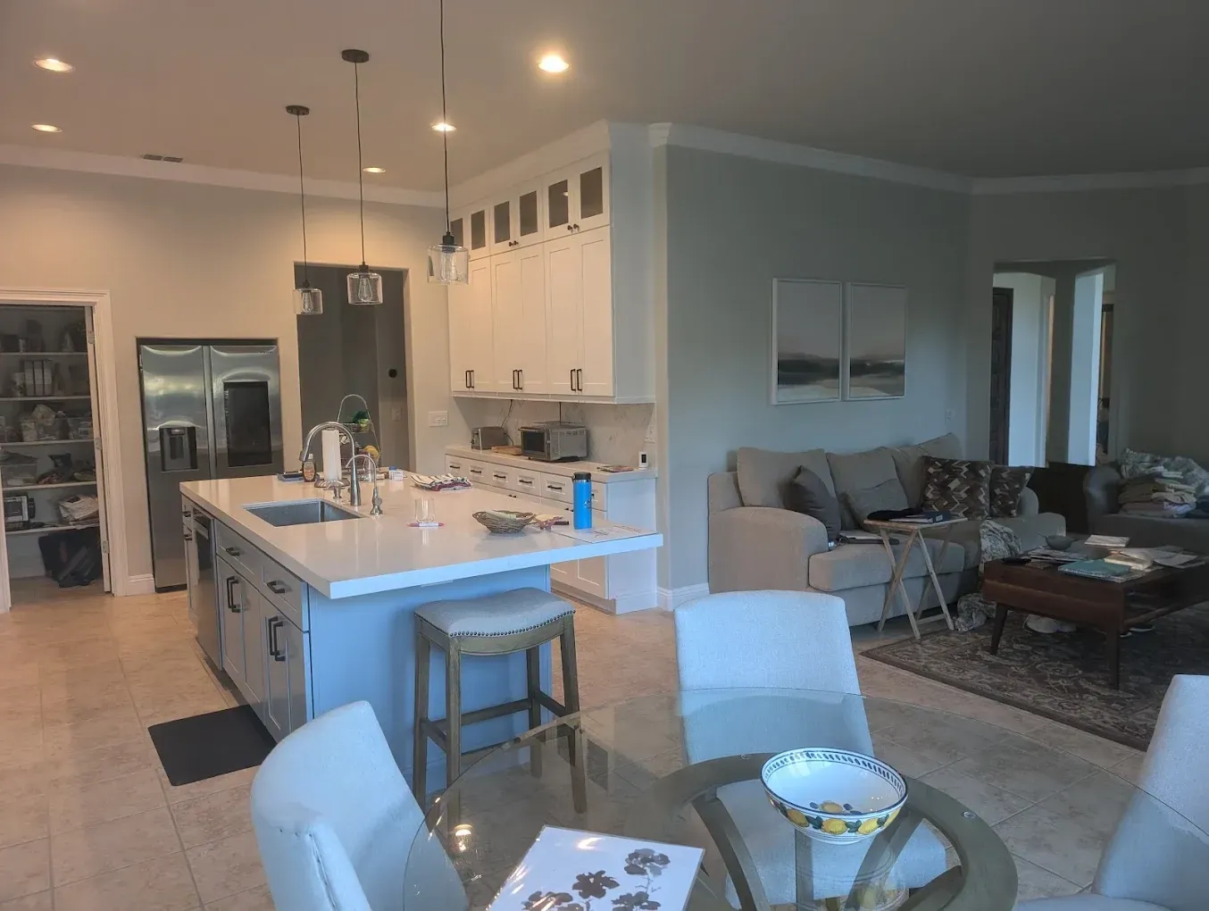 Kitchen with island, dining area, and living room. White cabinets, light blue island, chairs, beige floor, and gray walls.