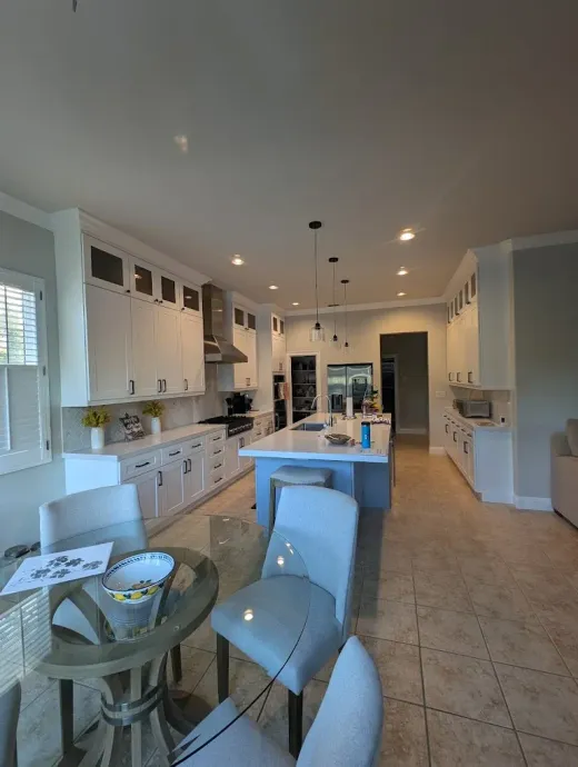 Spacious white kitchen with blue island, pendant lights, and light blue chairs surrounding a table.