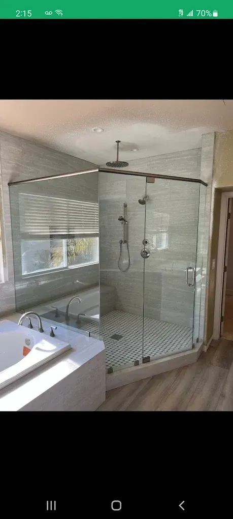 A modern bathroom with a glass-enclosed shower, bathtub, and light-colored tile and flooring.