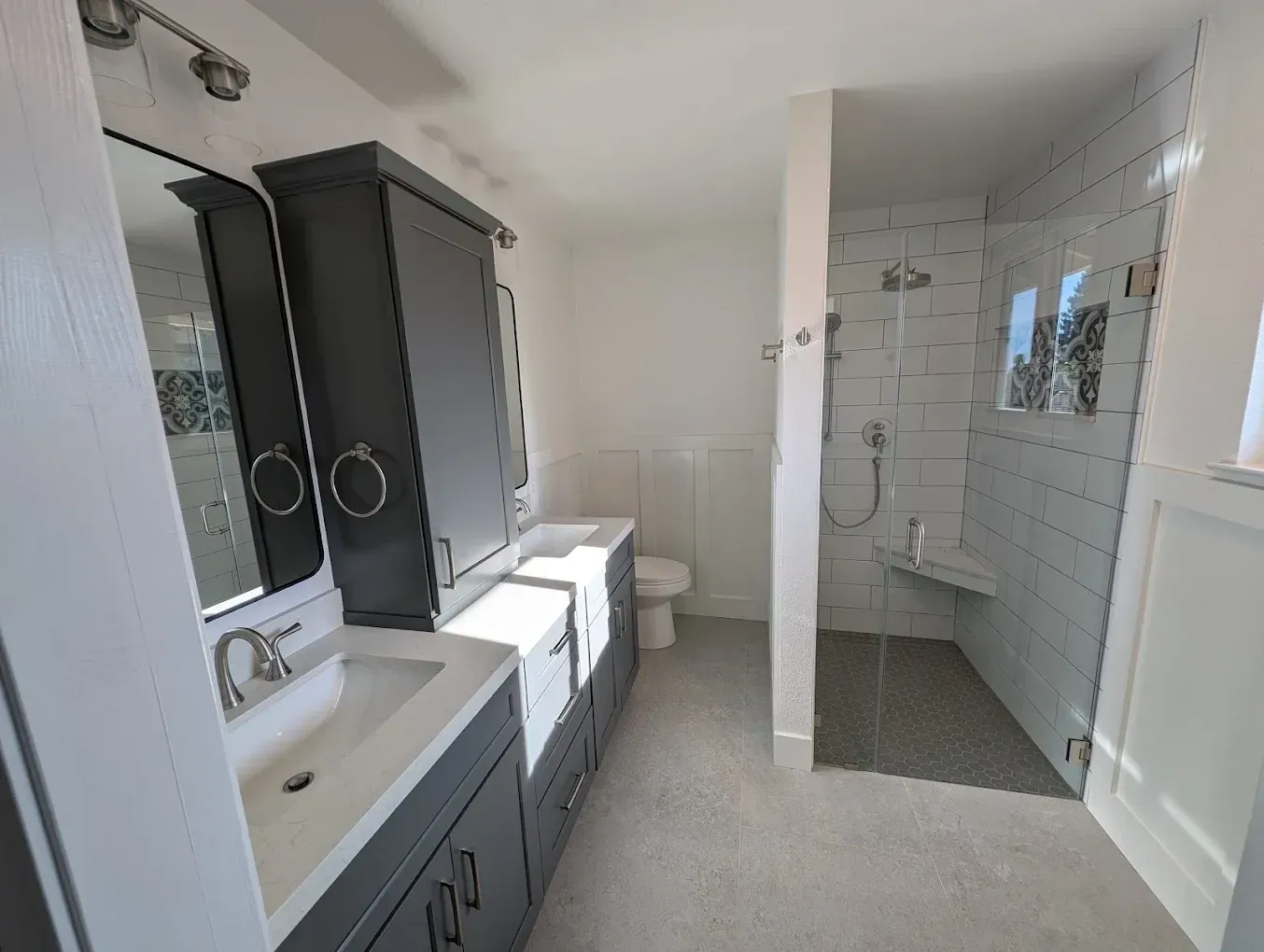 Modern bathroom with grey cabinets, white walls, and a tiled shower.