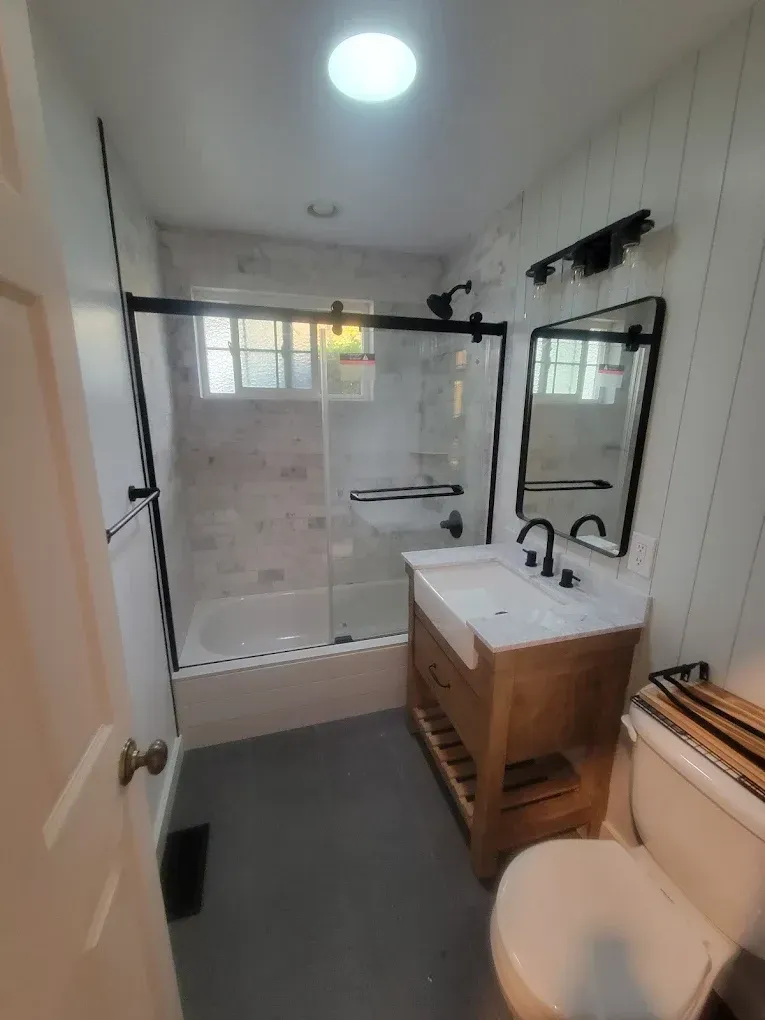 Bathroom with white walls, gray floor, glass shower, wooden vanity, and toilet.