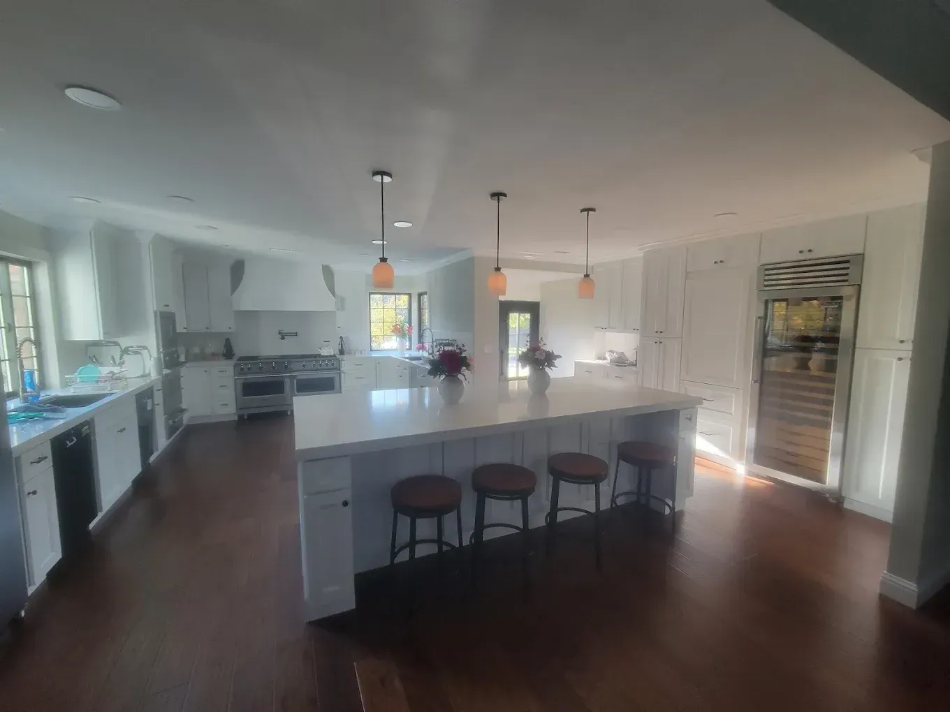 Spacious white kitchen with island, pendant lights, and brown leather bar stools, dark hardwood floors.