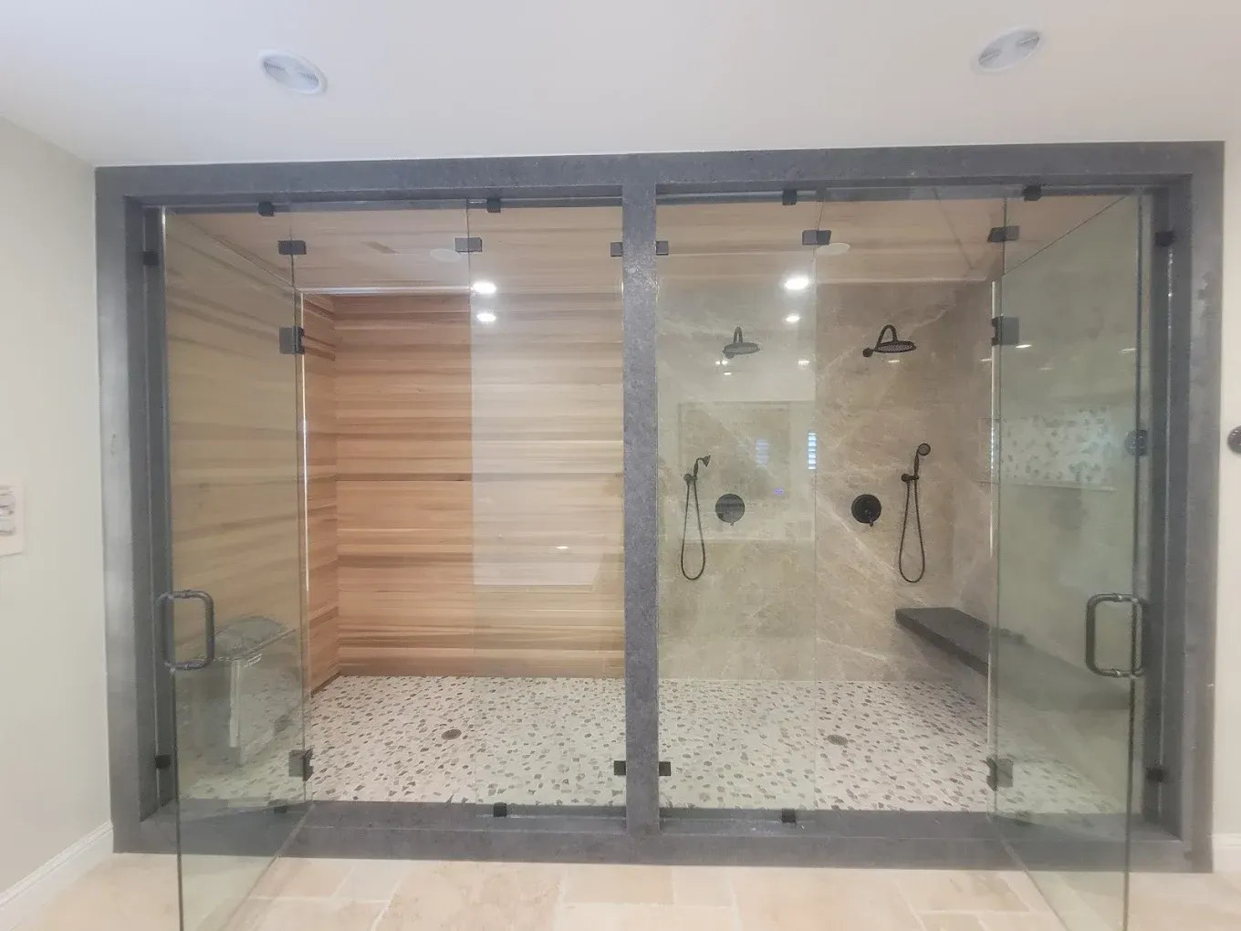 Two-stall shower with glass doors. One stall has wood paneling, the other has stone tile and shower fixtures.