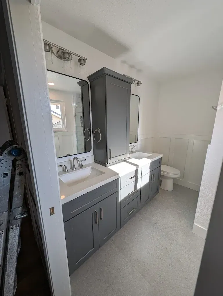Gray bathroom vanity with two sinks, a tall cabinet, and a toilet.