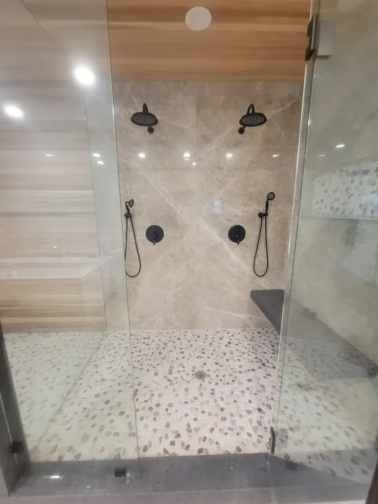 Dual shower with marble tile, pebble floor, and glass enclosure.