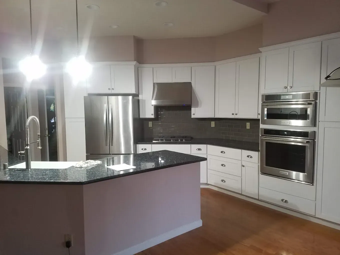 White kitchen with stainless steel appliances, dark countertops, and a granite island.