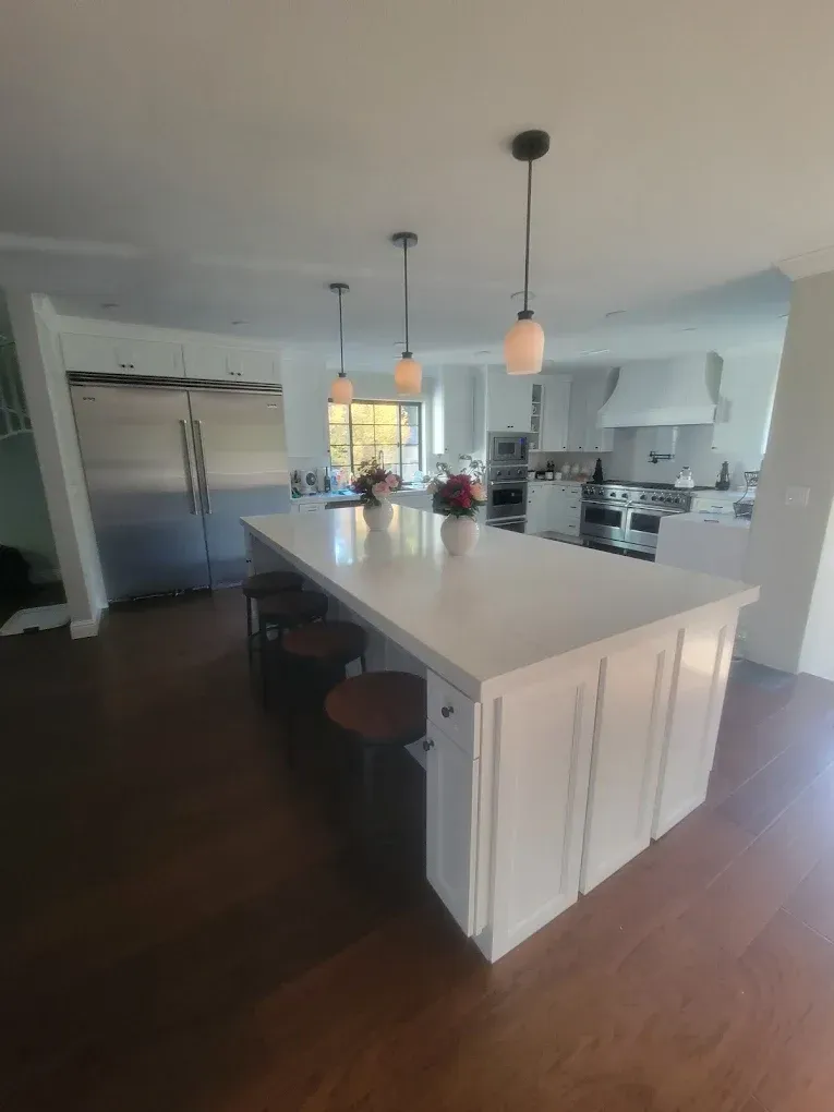Modern white kitchen with island, pendant lights, stainless steel fridge, and wood floors.