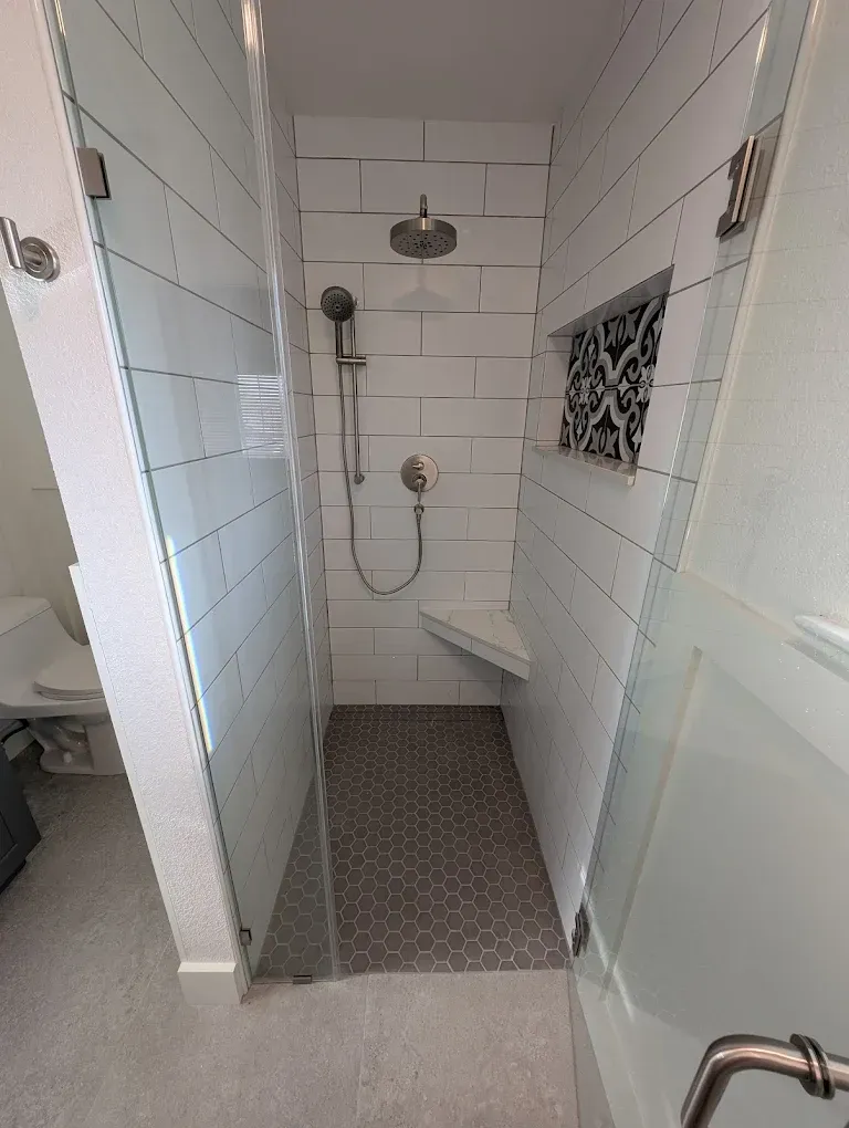 Modern shower with glass doors, white subway tile walls, and gray hexagonal floor tiles.