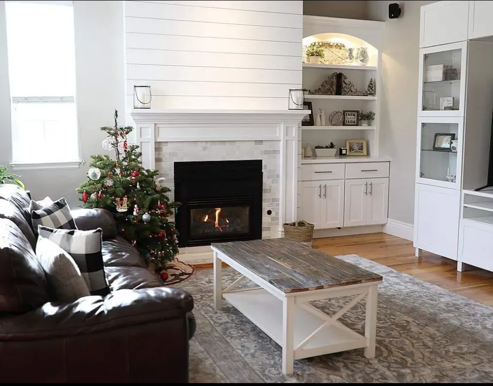 Living room with fireplace, Christmas tree, leather sofa, and white cabinetry.
