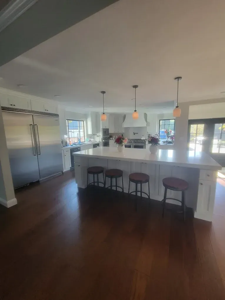 Spacious kitchen with large island, stainless steel fridge, dark wood floors, and pendant lights.