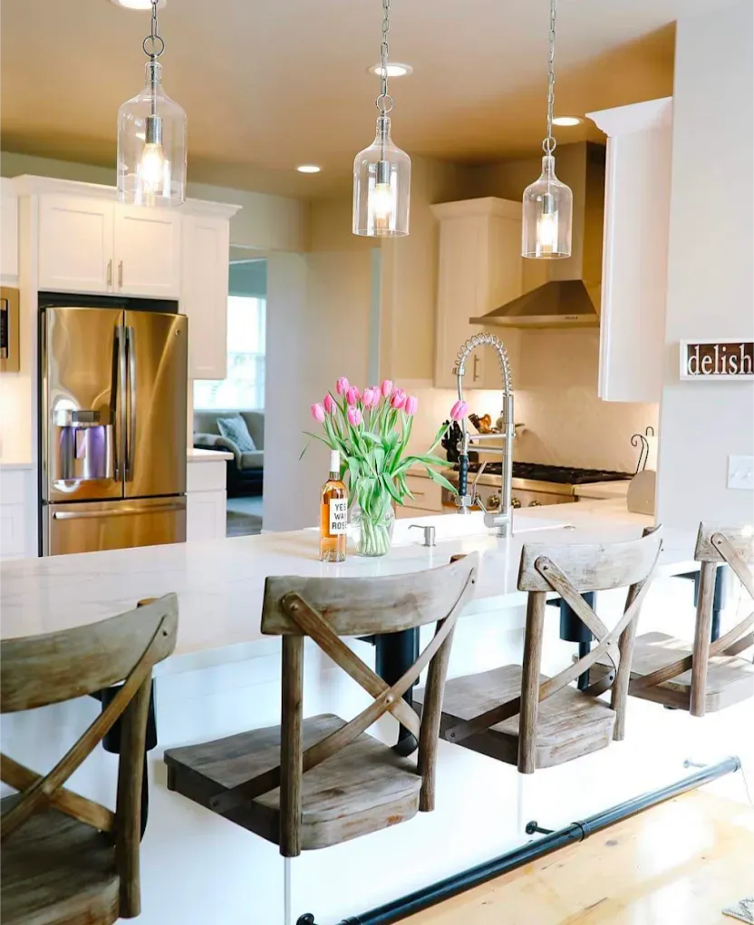 Kitchen island with three wooden chairs, clear pendant lights, and a stainless steel refrigerator.