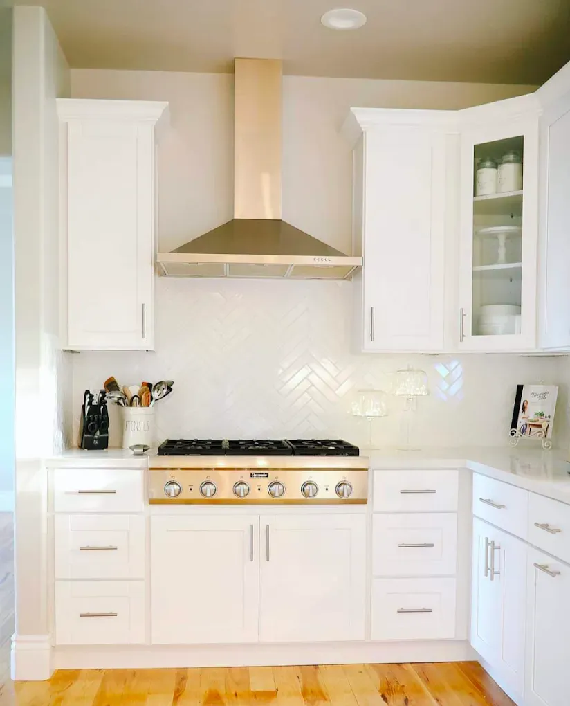 White kitchen with stainless steel range hood, cabinetry, and a white tile backsplash.