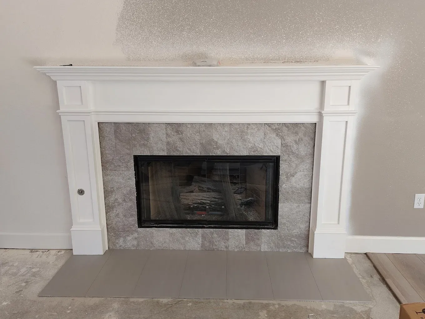 White fireplace mantel with gray stone tile surround and black fire screen.