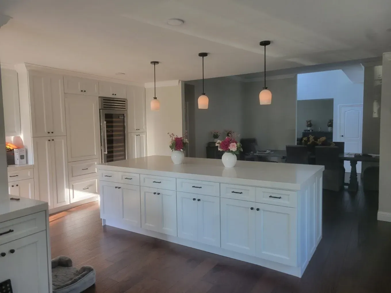 White kitchen with a large island, dark wood floors, and pendant lights.