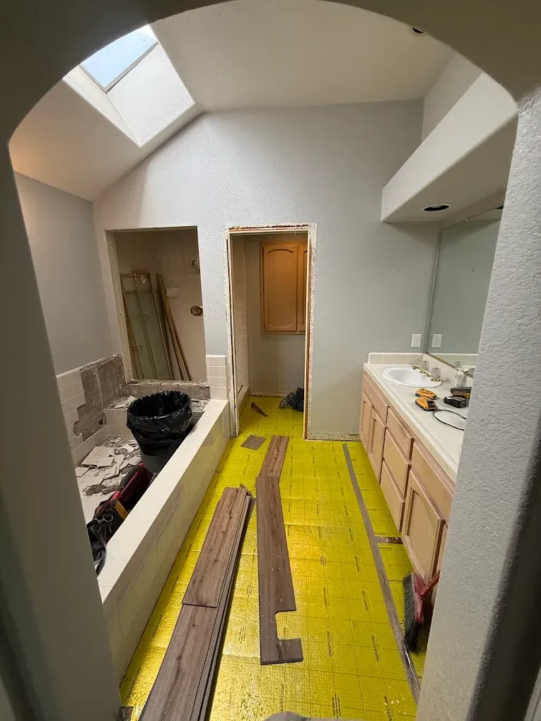 Bathroom under renovation, with tub, vanity, and flooring partially installed. Yellow underlayment visible.
